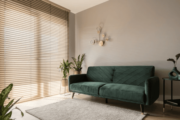 A modern living room featuring elegant wooden blinds, a stylish green velvet sofa, and indoor plants, creating a warm and inviting ambiance.