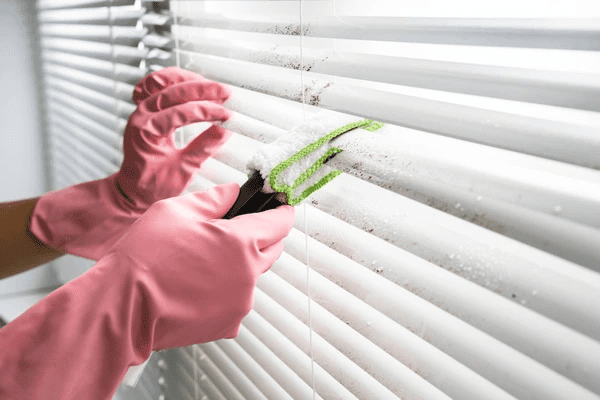 Close-up of hands in pink gloves using a specialized cleaning tool to remove dust from white blinds, demonstrating an effective DIY blind cleaning method in Dubai 2025.