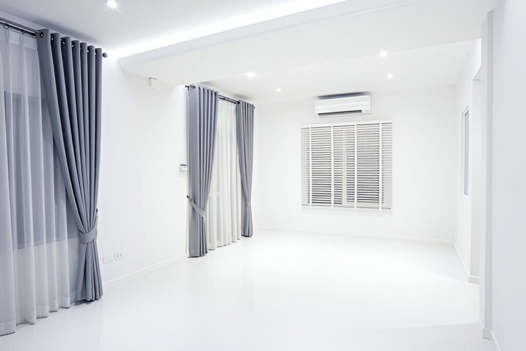 A bright, minimalistic room featuring sleek gray blackout curtains, sheer drapes, and stylish white blinds.
