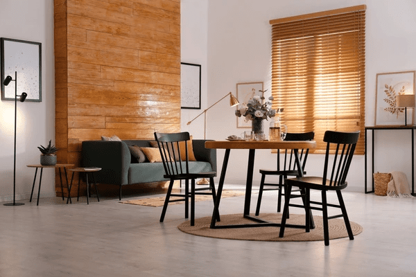  A modern dining room featuring a wooden table, black chairs, and elegant wooden blinds, enhancing the warm interior with best and cheap wooden blinds 2025 in Dubai.