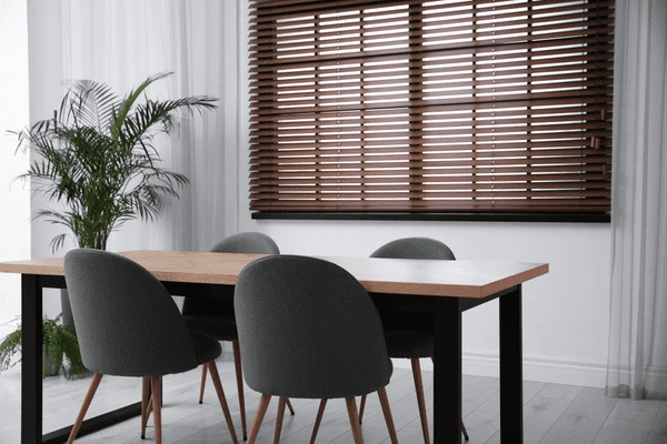 A modern dining room with a wooden table, gray chairs, and roman blind 2025 best and cheap, creating a sleek and elegant look.