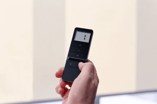 A person using a remote control to adjust top-rated motorized blinds in 2025, offering an affordable and cheap smart home solution.