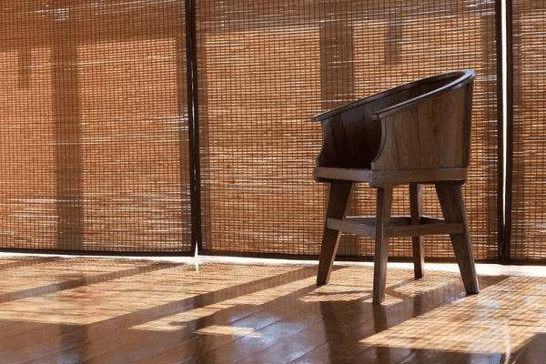 Sunlight streaming through stylish bamboo blinds, casting warm shadows on a wooden floor with a classic wooden chair.