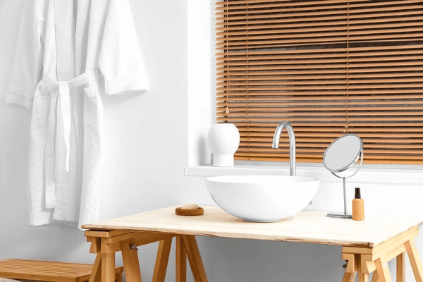 A modern bathroom with a stylish wooden countertop sink, a minimalist mirror, and warm wooden blinds providing privacy and elegance.