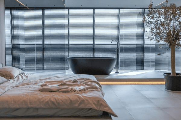 A luxurious modern bedroom with floor-to-ceiling window blinds, featuring a sleek black freestanding bathtub, showcasing the best privacy-focused and trendy window blinds in Dubai for 2025.