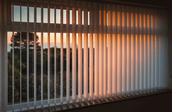 White vertical blinds on a bay window, filtering warm sunset light while offering a sleek and modern aesthetic.