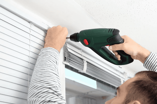 A man installing white Venetian blinds using a power drill, ensuring a secure and professional fit. The blinds offer a modern, stylish, and functional window covering for homes and offices in Dubai.