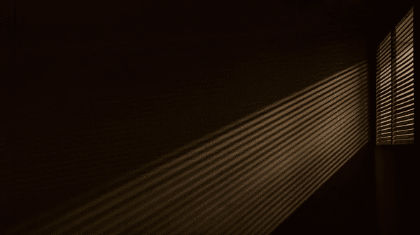 Dramatic light rays passing through window blinds in a dark room, showcasing effective sunlight control and eye strain reduction in Dubai interiors.

