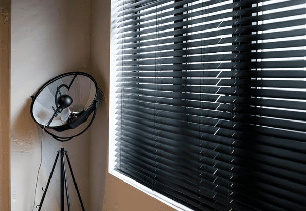 Stylish black window blinds providing sunlight protection and reducing eye strain, paired with a contemporary tripod lamp for a modern interior in Dubai.