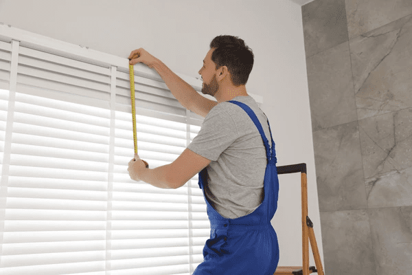 A professional installer in a blue uniform resizing and installing cut size blinds for a perfect window fit in Dubai.