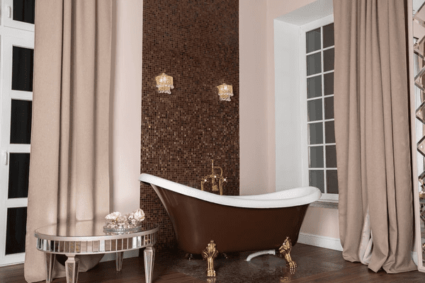  A luxurious bathroom featuring a vintage clawfoot bathtub, rich brown mosaic wall, elegant beige curtains, and opulent gold accents, creating a sophisticated and timeless ambiance.