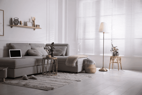 A cozy living room with a grey sectional sofa, soft lighting, and luxurious white blinds, creating a sleek and elegant ambiance in Dubai.