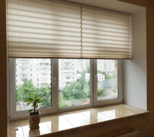 Elegant beige honeycomb blinds partially covering a large window, offering energy efficiency, light control, and a modern look in a Dubai apartment.