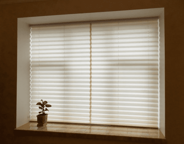 A window with stylish beige pleated blinds, diffusing natural light and creating a soft, modern ambiance, complemented by a small potted plant on a marble windowsill.