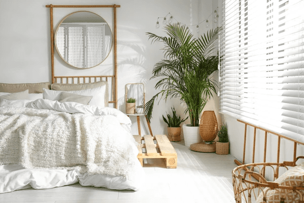 A bright, stylish bedroom with white light-filtering blinds, natural wood furniture, and lush green plants.