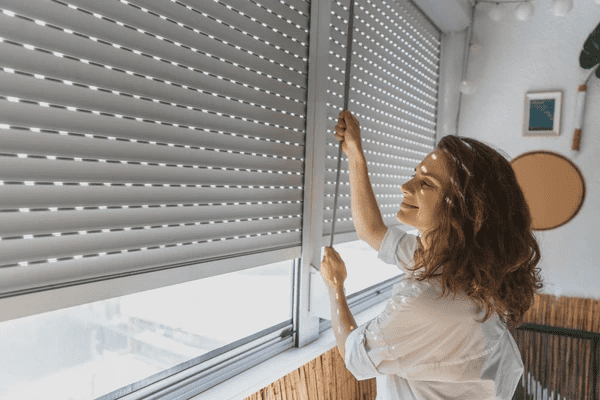 A young woman smiling while adjusting sleek, modern light-filtering blinds in a stylish, well-lit home.