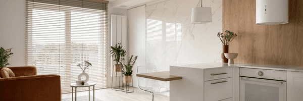 A modern open-plan living room and kitchen featuring elegant wooden Venetian blinds, offering the perfect blend of natural light control and privacy—part of the best living room & kitchen blinds Dubai 2025 collection.