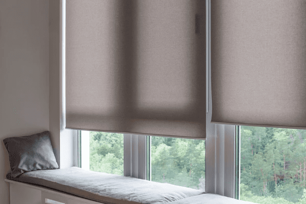 Cozy window nook with high-quality fabric roller blinds, providing privacy and blocking sunlight while complementing the modern interior with a soft, neutral tone.