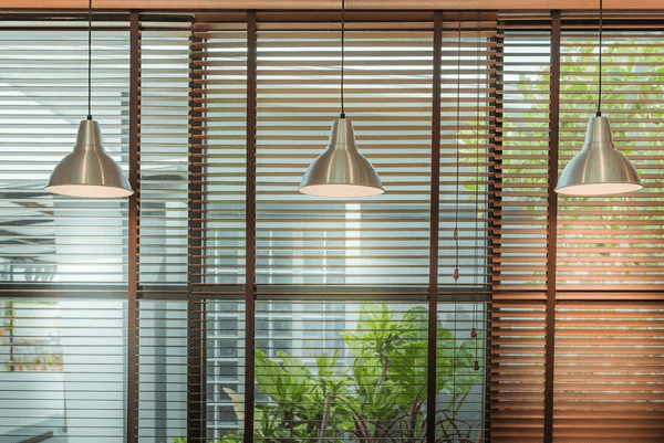 A stylish set of repaired and recycled Venetian blinds covering large glass windows, complemented by three industrial pendant lights, creating a modern and eco-friendly interior.