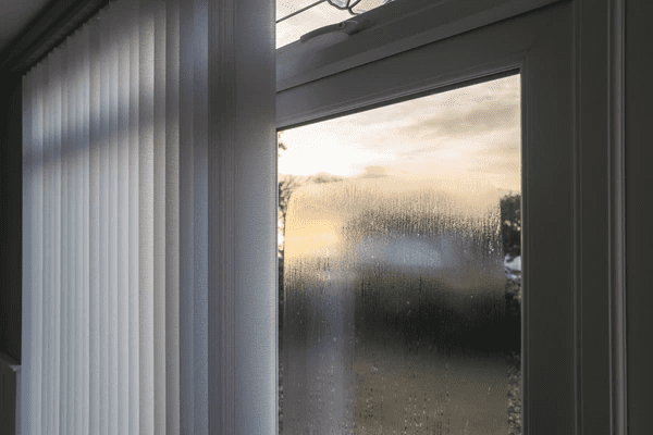 A double-glazed window with condensation forming on the glass, partially covered by modern vertical blinds, ideal for reducing moisture and improving insulation in Dubai 2025 homes.