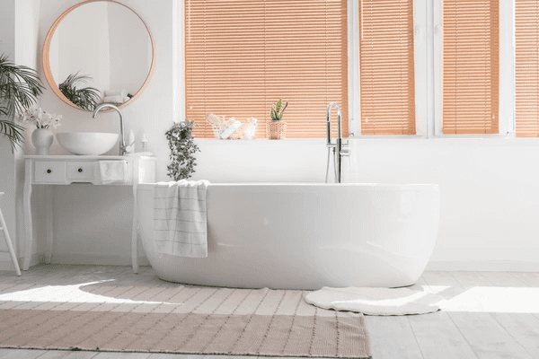 Elegant wooden blinds in a modern bathroom, enhancing the sleek and luxurious ambiance. A freestanding bathtub, white vanity, and greenery complement the sophisticated aesthetic.