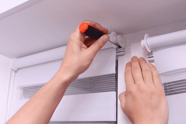 A close-up view of hands installing zebra roller blinds using a screwdriver, ensuring a secure and professional finish for a modern window treatment.