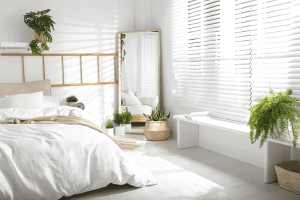Bright modern bedroom with white wooden blinds, indoor plants, a floor mirror, and cozy bedding in a Dubai home.