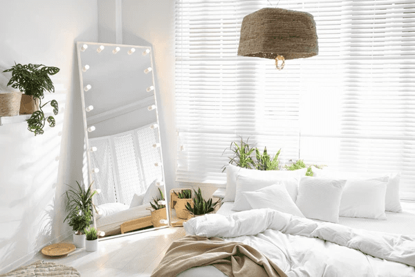 Stylish Dubai bedroom with sleek white venetian blinds, large mirror with lights, and cozy white bedding.