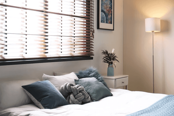 Cozy Dubai bedroom with stylish wooden venetian blinds, soft pillows, a bedside table, and ambient lighting.