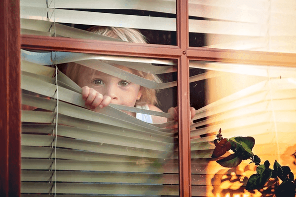 Young child peeking through flexible window blinds, illustrating the best blinds for children to choose in Dubai 2025—modern, safe, and cozy for playful homes.