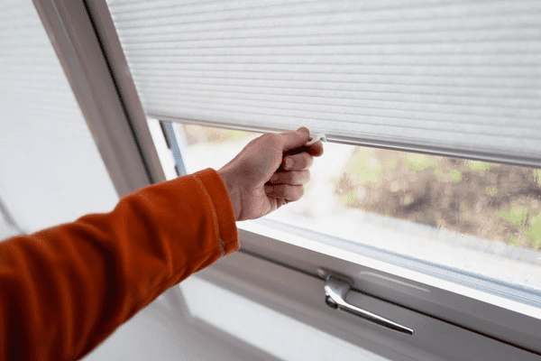 A person in an orange sleeve adjusting sleek cordless blinds on a conservatory window.