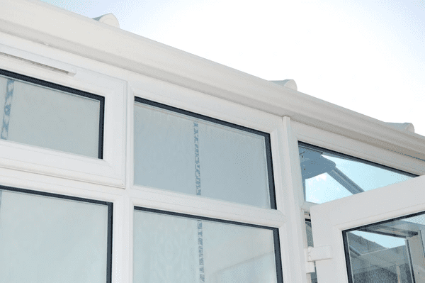 Close-up view of conservatory windows with frosted or privacy blinds installed on white-framed glass panels.