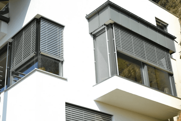 A contemporary home exterior with sleek, metallic horizontal blinds covering large corner and side conservatory windows.