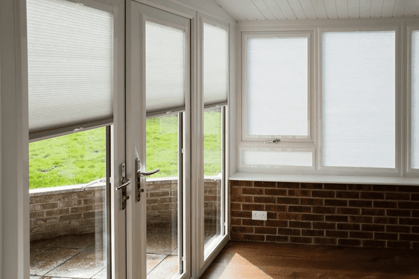 White light-filtering blinds on patio doors and windows in a bright sunroom with brick and wood accents.