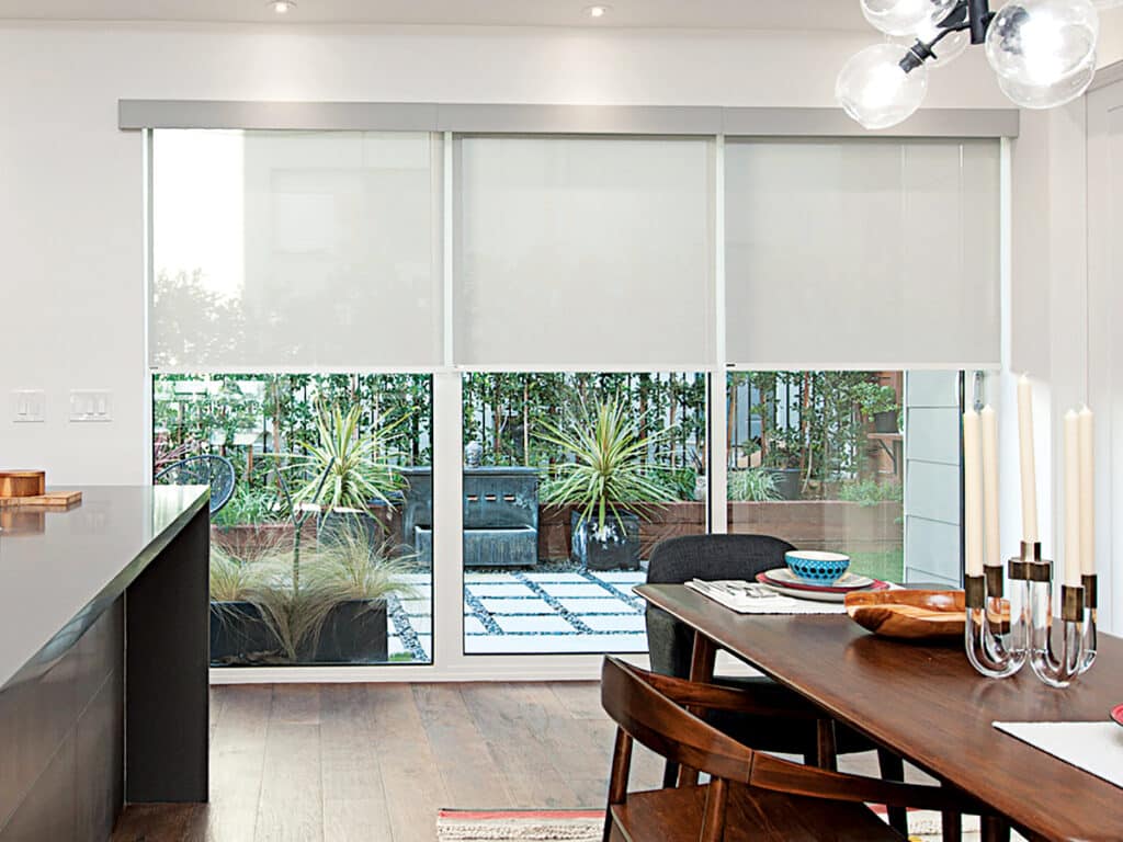 Modern dining area featuring sleek roller blinds on wide patio doors, overlooking a stylish outdoor garden space.