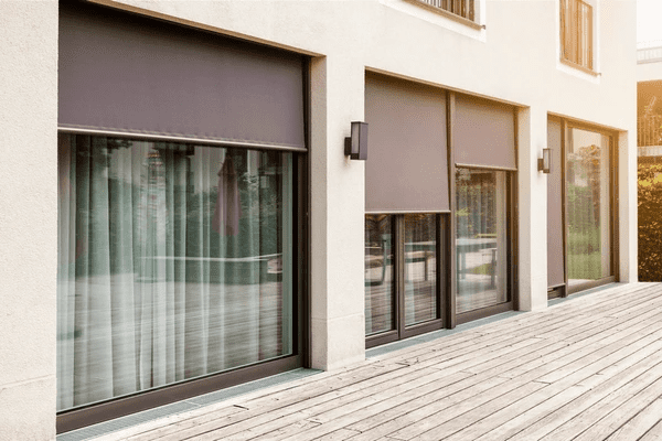 Modern outdoor roller blinds on large patio doors and windows of a contemporary home with a wooden deck.