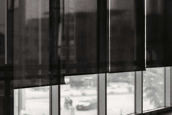 Close-up of sleek black blinds in a modern room with large glass windows overlooking an urban cityscape.