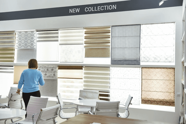 A woman browsing a new collection of discounted blinds and shades at a modern Dubai showroom with various sleek designs on display.