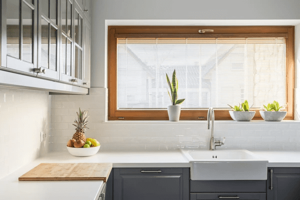 A cozy Dubai kitchen in 2025 with natural wooden frame blinds, modern grey cabinets, and indoor plants on a white countertop.