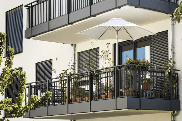 Modern apartment balcony with outdoor black blinds, potted plants, and a white umbrella.