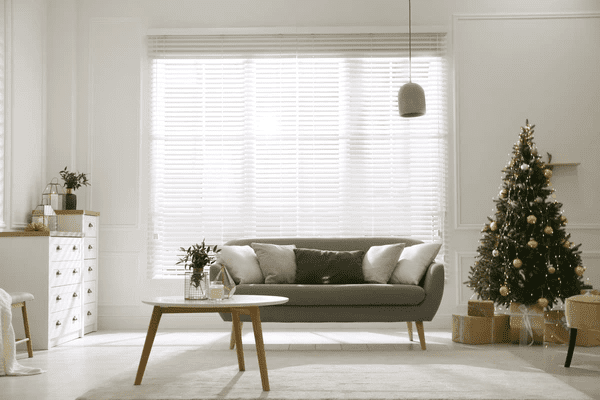 A bright living room with white blinds, a modern sofa, and a beautifully decorated Christmas tree, creating a warm and stylish holiday ambiance.