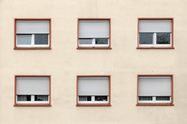 Beige building exterior featuring six windows with sleek white outdoor roller blinds partially closed.