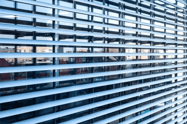 Modern outdoor metal louver blinds on a glass building facade reflecting the city skyline in Dubai.