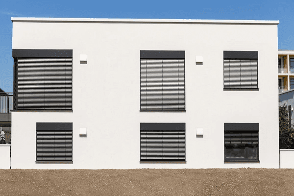 White modern house facade with multiple large windows fitted with black horizontal outdoor blinds, under a clear blue sky in Dubai.White modern house facade with multiple large windows fitted with black horizontal outdoor blinds, under a clear blue sky in Dubai.