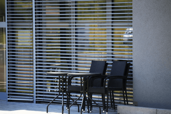 Outdoor silver venetian blinds with a black patio set in front of a modern glass wall in Dubai.