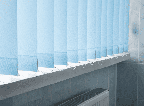 Light blue painted vertical blinds over a window in a tiled room, softly filtering daylight.