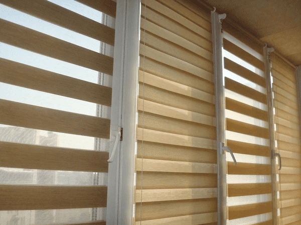 Close-up of beige zebra blinds on tall windows, alternating sheer and solid stripes allowing soft filtered sunlight.