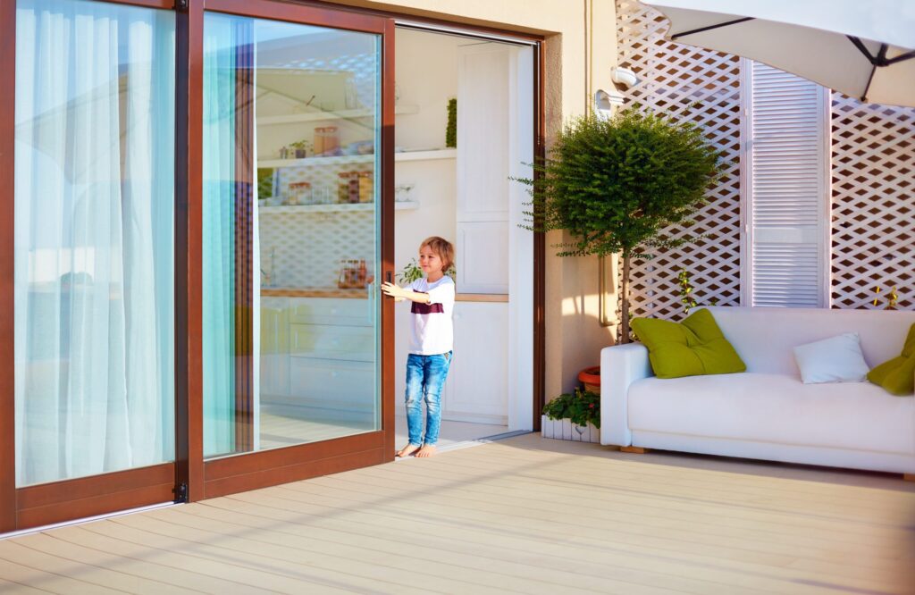 A child playing near modern sliding glass patio doors with a cozy outdoor seating area.