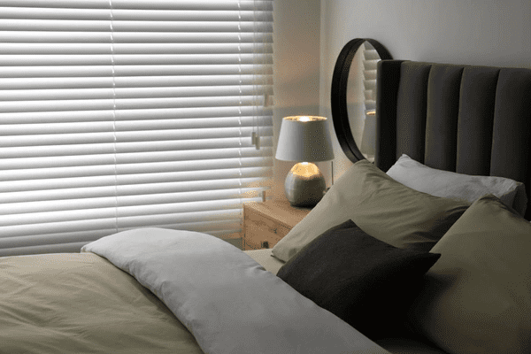 A stylish bedroom in Dubai featuring horizontal blinds, a plush bed, and a bedside lamp for a cozy ambiance.