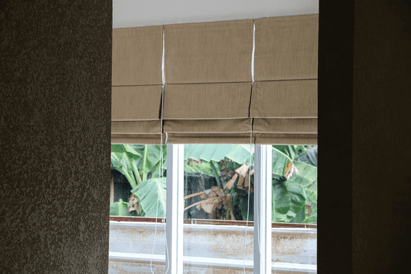 Light brown recycled Roman blinds on a white-framed window with a garden view, creating a sleek and eco-conscious interior look.